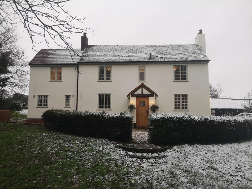 Large white cottage with olive green windows and wooden door decorated by SM Decorators in Essex