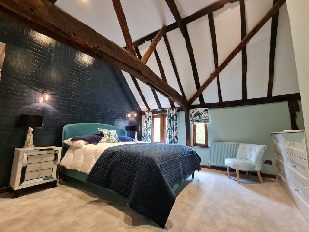 Bedroom with exposed wooden beams and blue painted brick feature wall decorated by SM Decorators in Essex